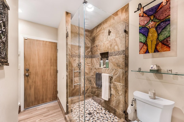 bathroom featuring hardwood / wood-style flooring, a shower with door, and toilet