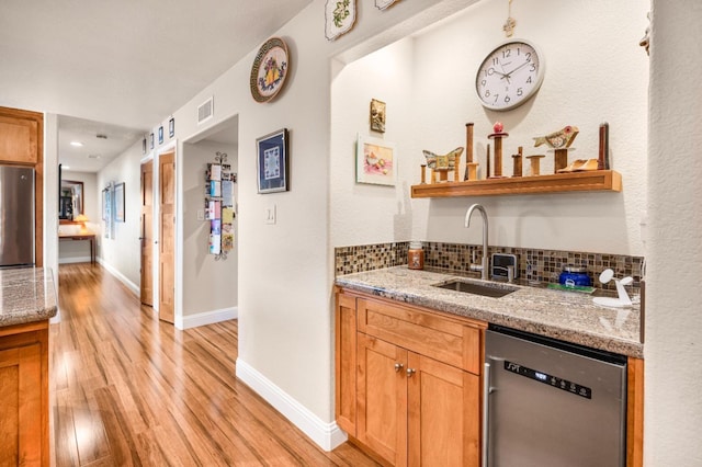 bar featuring decorative backsplash, light stone countertops, stainless steel appliances, sink, and light hardwood / wood-style floors