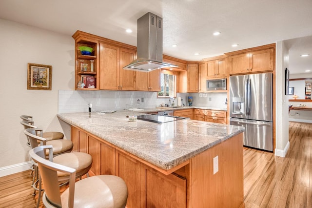 kitchen featuring island exhaust hood, appliances with stainless steel finishes, kitchen peninsula, and a breakfast bar area