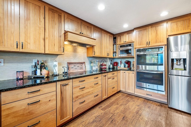 kitchen featuring hardwood / wood-style floors, stainless steel appliances, tasteful backsplash, and dark stone countertops