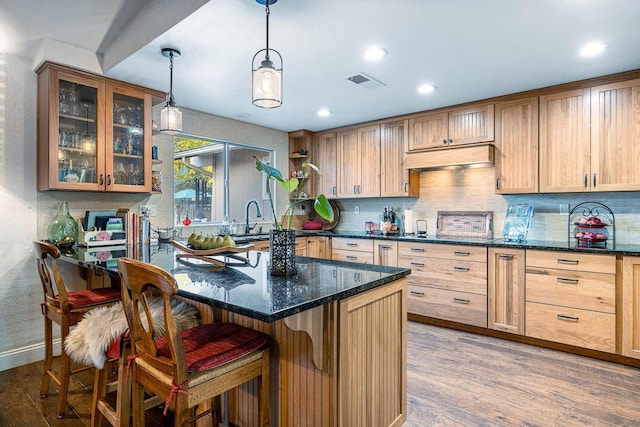 kitchen featuring tasteful backsplash, hardwood / wood-style flooring, dark stone countertops, hanging light fixtures, and a breakfast bar area