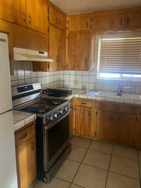 kitchen with tile countertops, tasteful backsplash, sink, and stainless steel range with gas stovetop