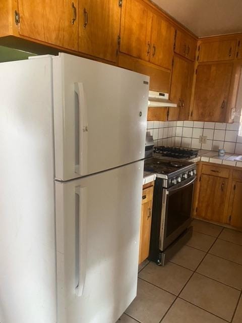 kitchen with backsplash, light tile patterned floors, range with gas cooktop, and white refrigerator