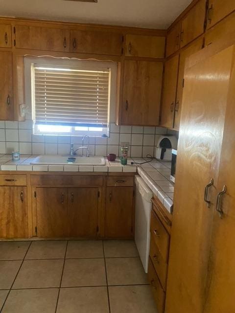 kitchen with white dishwasher, tile counters, light tile patterned floors, and sink