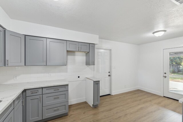 kitchen featuring a textured ceiling, backsplash, light hardwood / wood-style flooring, and gray cabinetry