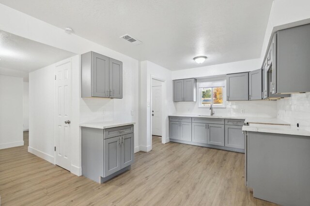 kitchen featuring light wood-type flooring, tasteful backsplash, gray cabinetry, and sink