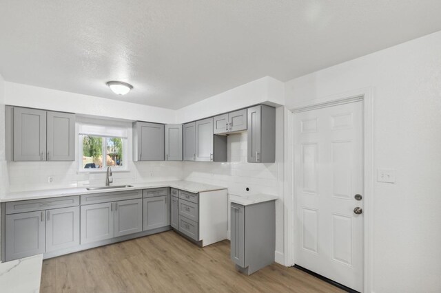 kitchen featuring backsplash, gray cabinets, light hardwood / wood-style floors, and sink