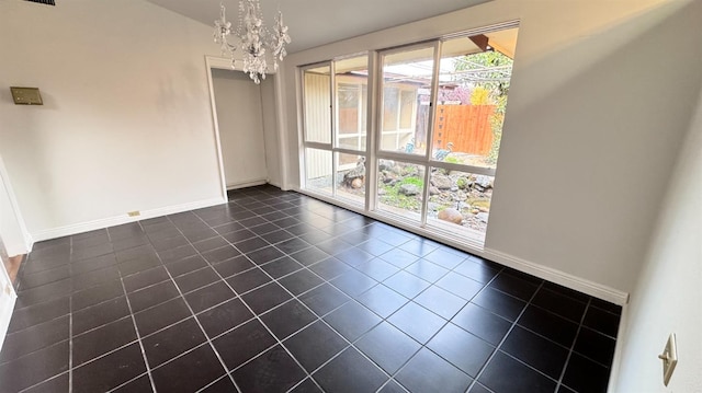 spare room with a notable chandelier, dark tile patterned flooring, and a wealth of natural light