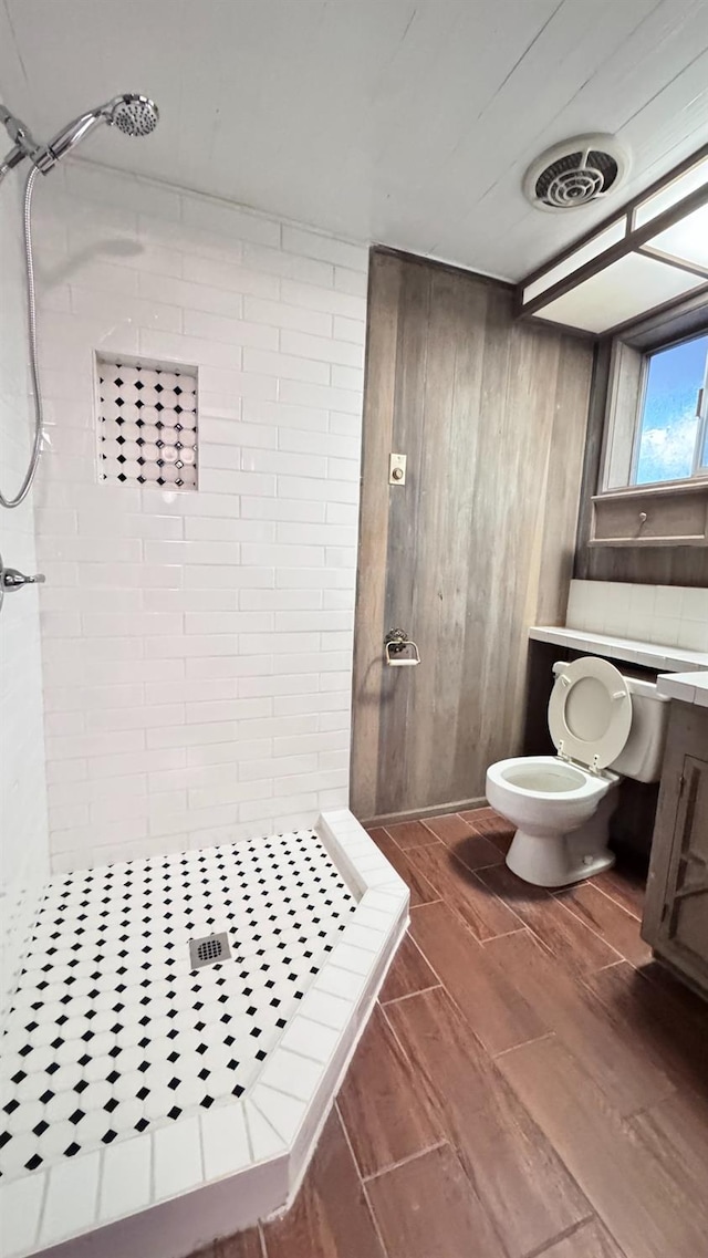 bathroom with a tile shower, toilet, and wood walls