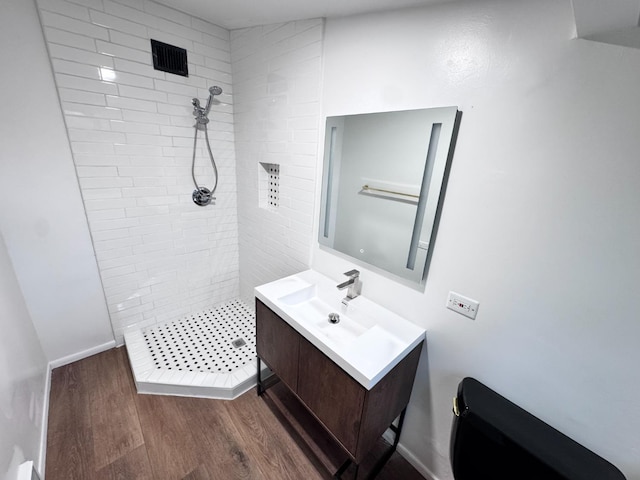 bathroom featuring hardwood / wood-style flooring, vanity, toilet, and a tile shower