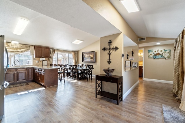 5870 E Midwick Ln, Fresno, CA 93727 - kitchen featuring vaulted ceiling, a sink, light wood finished floors, a peninsula, and baseboards
