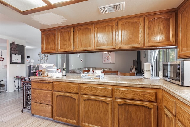 kitchen with tile counters, light wood-type flooring, and kitchen peninsula