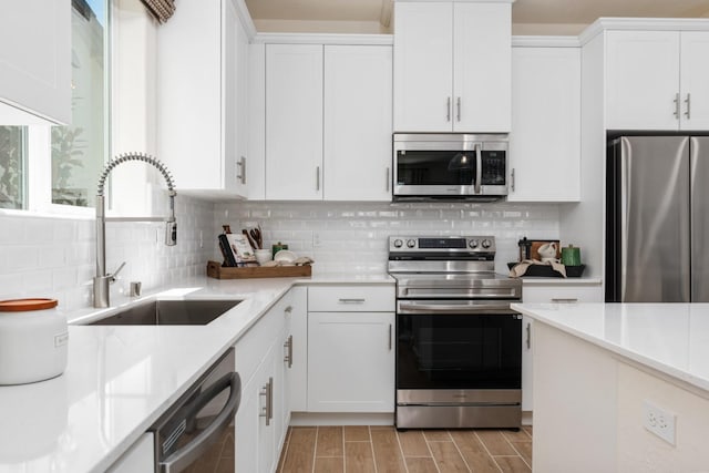 kitchen featuring wood tiled floor, a sink, white cabinets, appliances with stainless steel finishes, and backsplash