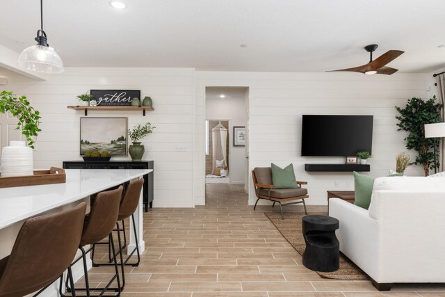 living room with ceiling fan, wooden walls, and light hardwood / wood-style floors