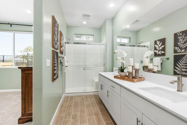 bathroom featuring visible vents, a shower stall, wood tiled floor, double vanity, and a sink