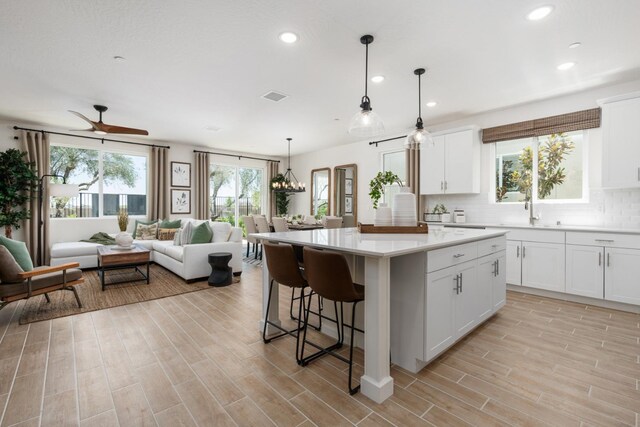 kitchen with hanging light fixtures, tasteful backsplash, white cabinets, a kitchen island, and ceiling fan with notable chandelier