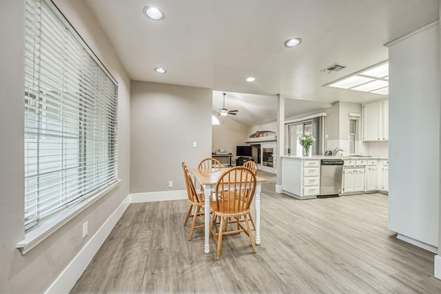 dining area with ceiling fan, a fireplace, vaulted ceiling, and light hardwood / wood-style flooring