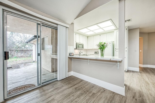 kitchen featuring white cabinetry, light hardwood / wood-style flooring, kitchen peninsula, white fridge, and a breakfast bar area