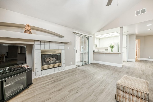 living room featuring ceiling fan, lofted ceiling, light hardwood / wood-style flooring, and a tiled fireplace