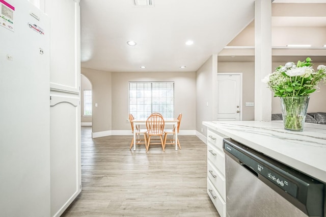 kitchen with light stone countertops, white cabinets, stainless steel dishwasher, and light hardwood / wood-style floors