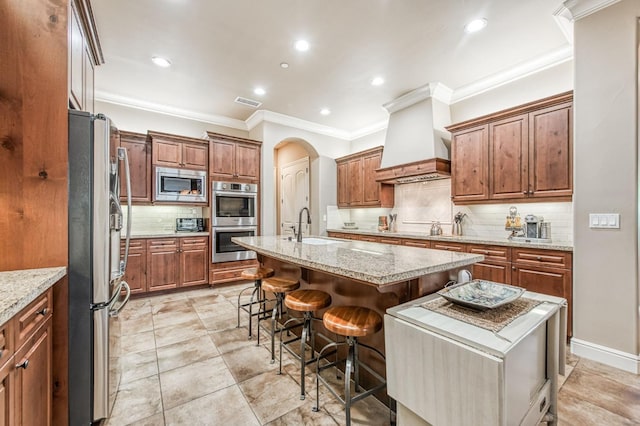 kitchen with sink, premium range hood, an island with sink, a breakfast bar, and appliances with stainless steel finishes