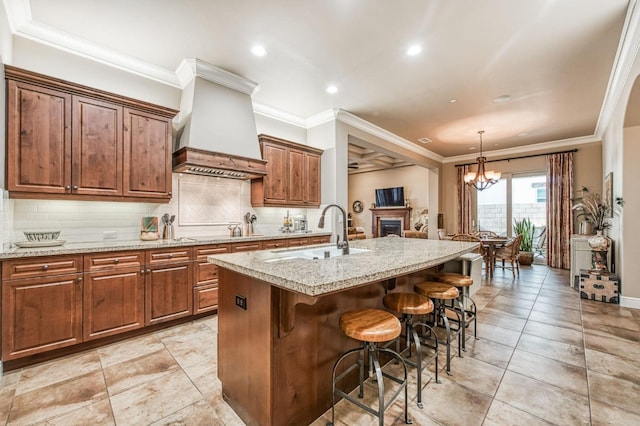 kitchen with sink, a breakfast bar area, a kitchen island with sink, custom range hood, and ornamental molding