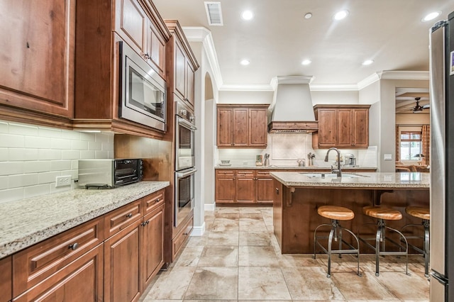 kitchen featuring a kitchen bar, light stone countertops, appliances with stainless steel finishes, ornamental molding, and custom range hood