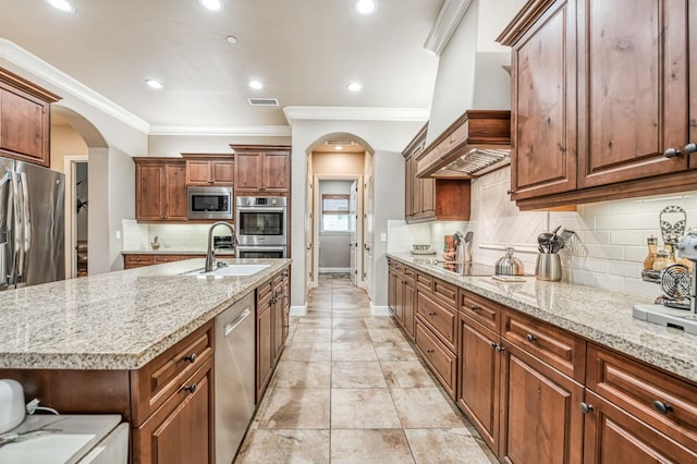 kitchen with light stone countertops, appliances with stainless steel finishes, crown molding, sink, and an island with sink