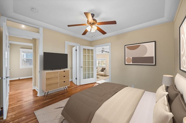 bedroom with hardwood / wood-style floors, a tray ceiling, french doors, and ceiling fan