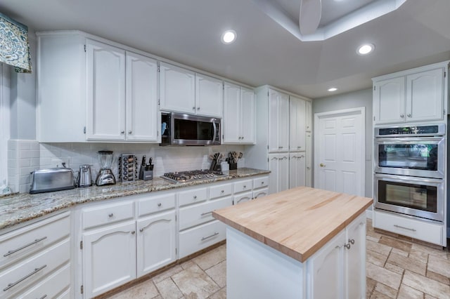 kitchen featuring decorative backsplash, light stone countertops, stainless steel appliances, white cabinets, and a center island