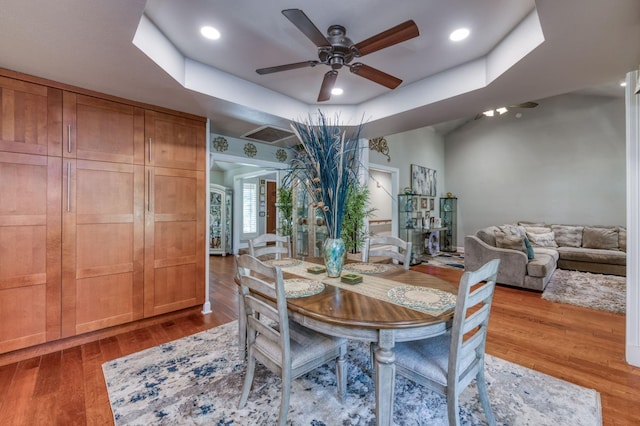 dining room featuring ceiling fan, a raised ceiling, and light wood-type flooring