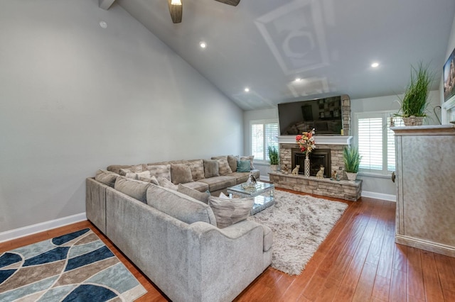 living room featuring a stone fireplace, ceiling fan, vaulted ceiling, and hardwood / wood-style flooring