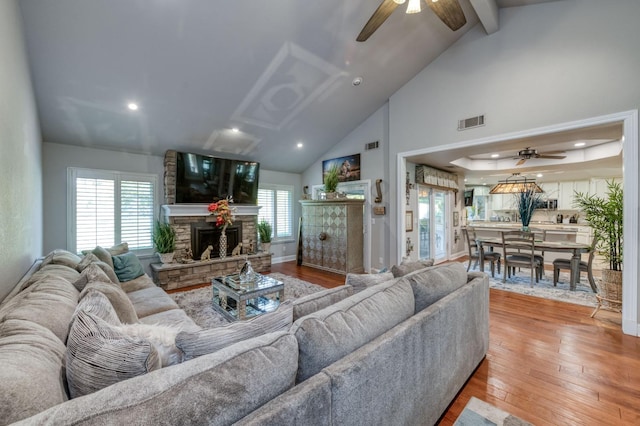 living room with a stone fireplace, ceiling fan, high vaulted ceiling, and wood-type flooring