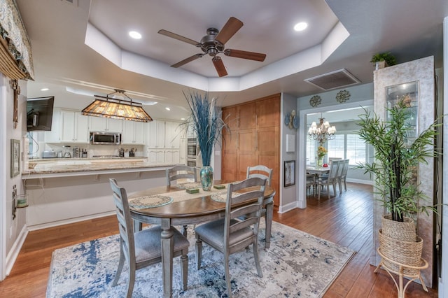 dining room with a raised ceiling, hardwood / wood-style floors, and ceiling fan with notable chandelier