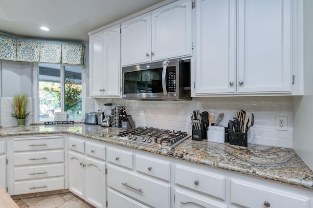 kitchen with backsplash, light stone countertops, white cabinetry, and stainless steel appliances