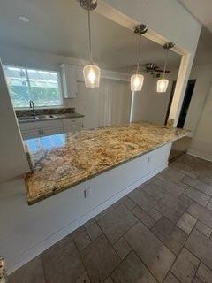 kitchen featuring decorative light fixtures, light stone countertops, white cabinetry, and sink