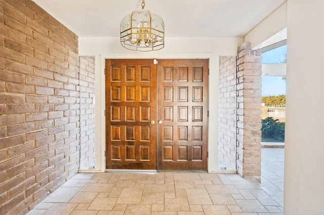 foyer entrance featuring brick wall and a notable chandelier