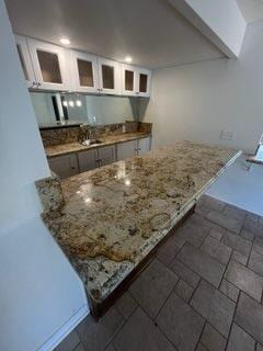 kitchen with white cabinets, light stone counters, kitchen peninsula, and sink