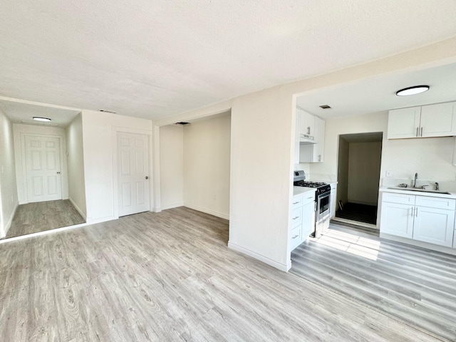 kitchen with stainless steel gas range oven, a textured ceiling, sink, light hardwood / wood-style floors, and white cabinetry