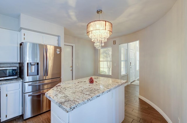 kitchen featuring light stone countertops, stainless steel appliances, pendant lighting, an inviting chandelier, and white cabinetry