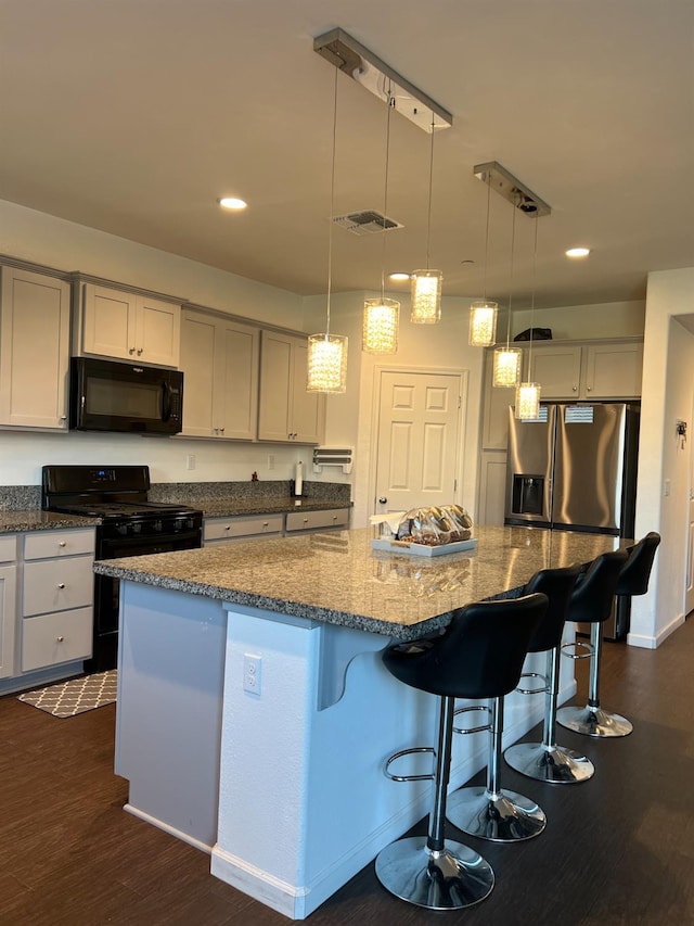 kitchen featuring a kitchen bar, dark wood-type flooring, black appliances, a center island, and hanging light fixtures