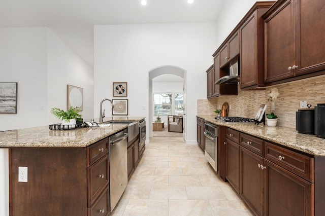 kitchen featuring light stone countertops, appliances with stainless steel finishes, decorative backsplash, and a kitchen island with sink