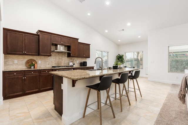 kitchen with light stone countertops, sink, wall chimney exhaust hood, a kitchen breakfast bar, and a kitchen island with sink