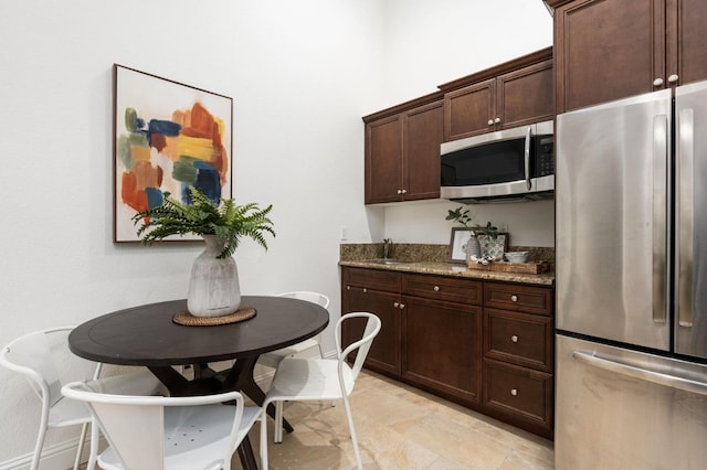 kitchen with appliances with stainless steel finishes, dark brown cabinets, dark stone counters, and sink