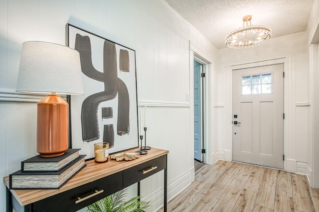 entrance foyer with crown molding, an inviting chandelier, a textured ceiling, and light wood-type flooring