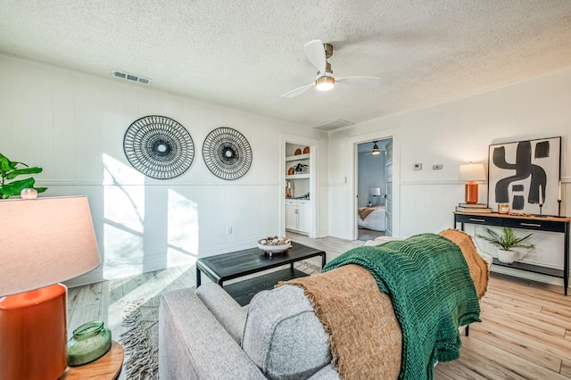 living room with a textured ceiling, light wood-type flooring, and ceiling fan