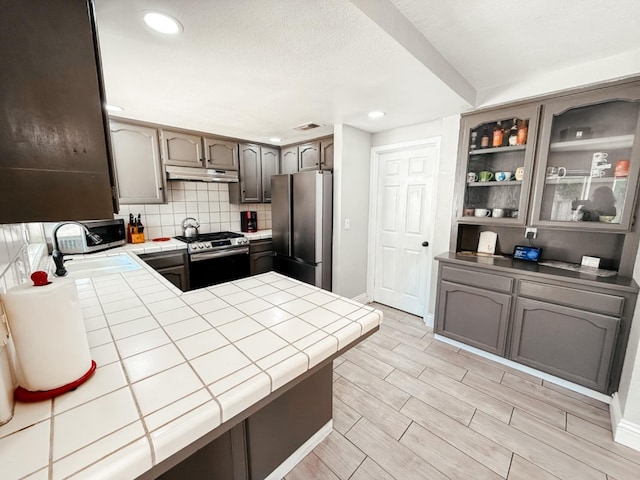 kitchen with kitchen peninsula, decorative backsplash, stainless steel appliances, sink, and tile counters