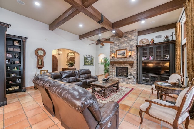 tiled living room with ceiling fan, beam ceiling, and a stone fireplace