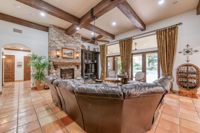 living room with ceiling fan, beam ceiling, a stone fireplace, and light tile patterned floors