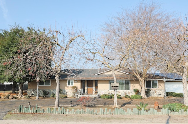 ranch-style home featuring stone siding, fence, and stucco siding